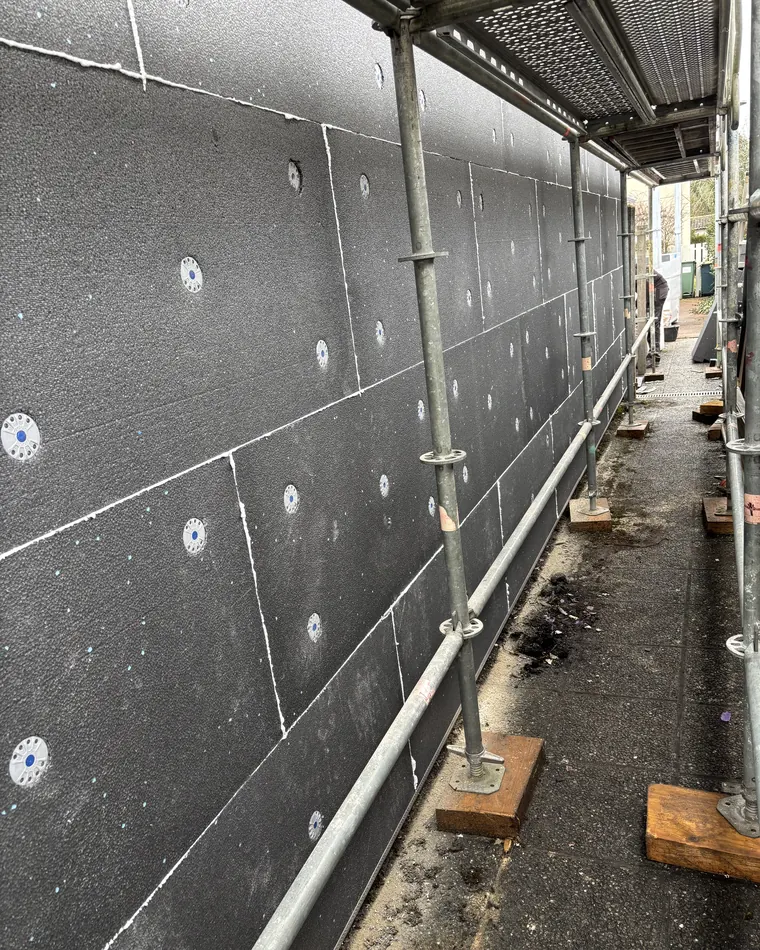 Panneaux isolants chevillés sur un mur de façade, derrière un échafaudage