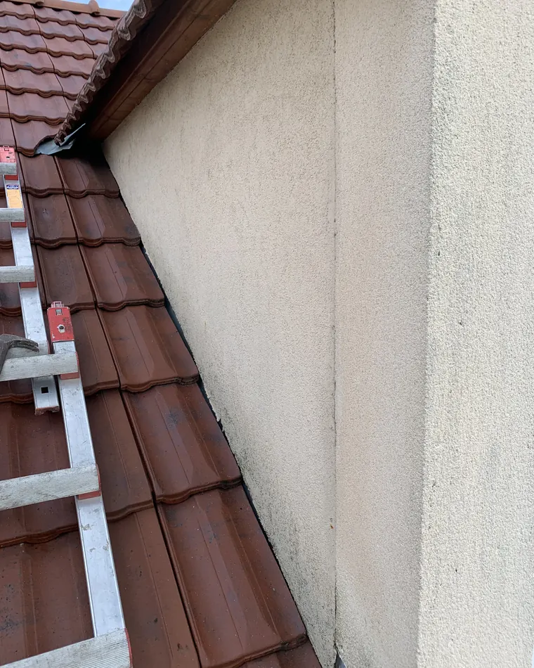 Rive d'une toiture en tuiles mécaniques contre un mur enduit